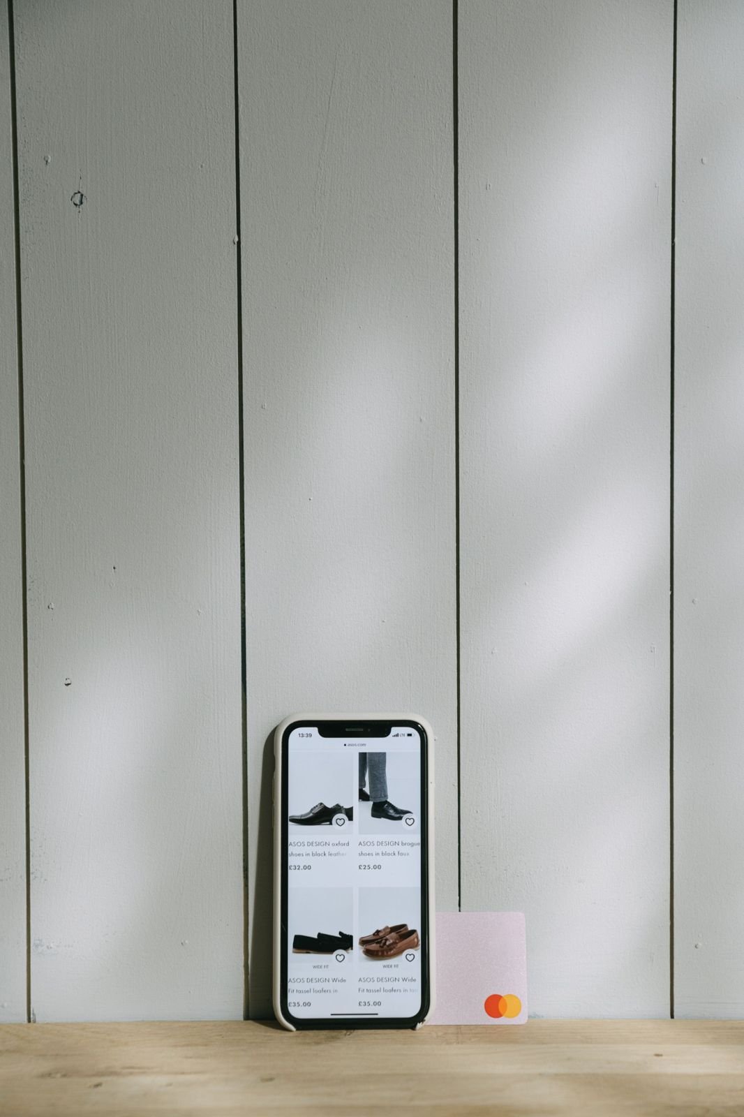 A phone showing an online shoe shop, propped against a panelled wall